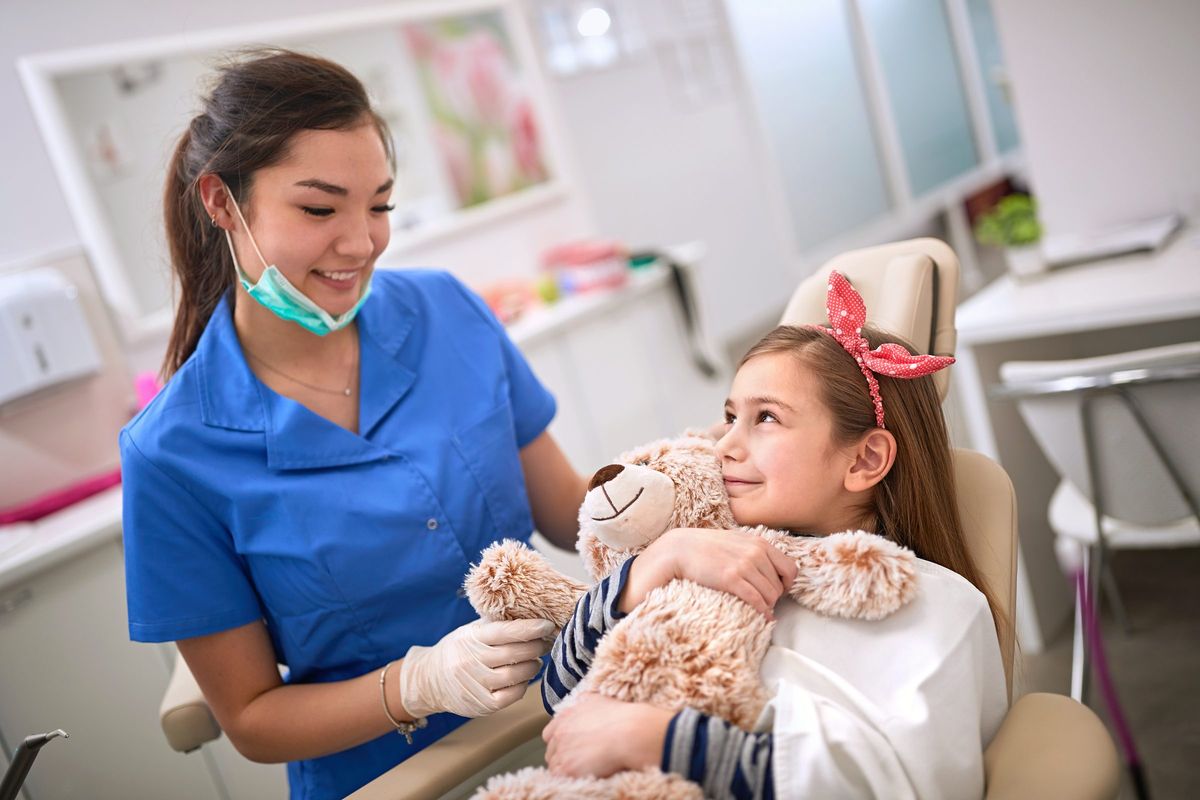 Dentist chatting with a young patient holding a teddy bear